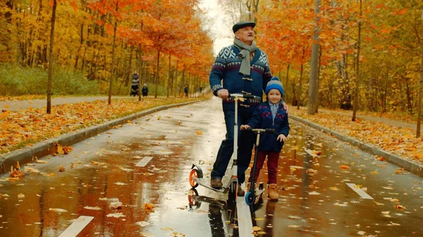 Niño y su abuelo están montando patinetas juntos en el parque de otoño —  Fotos de Stock