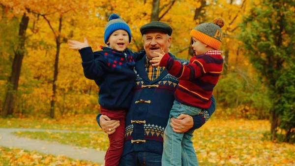 Glücklicher Opa hält zwei kleine Jungen im herbstlichen Wald auf dem Arm — Stockfoto