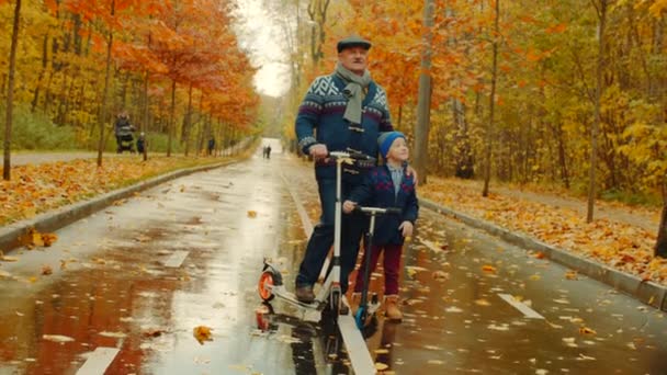 Niño y su abuelo están montando patinetas scooters en el parque de otoño — Vídeo de stock