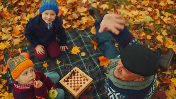 Il nonno sta insegnando ai nipoti a giocare a scacchi nel parco autunnale. — Video Stock