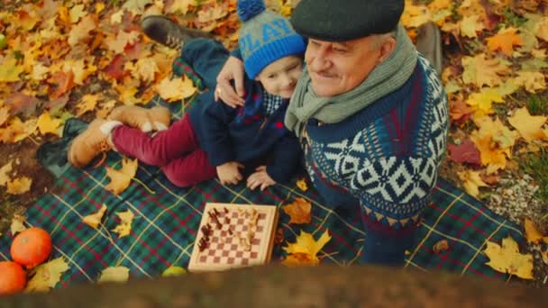 Dziadek uczy wnuka grać w szachy w parku jesień — Wideo stockowe