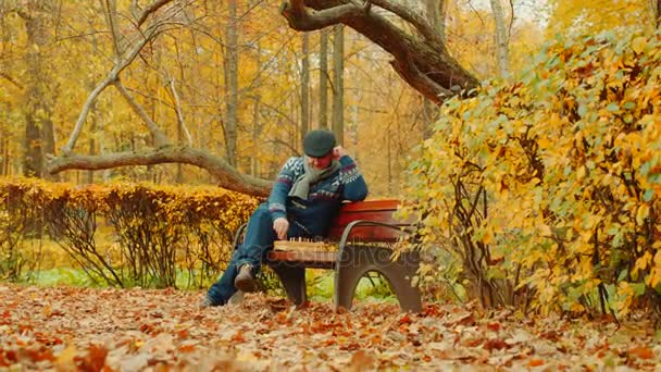 Stary człowiek jest gra w szachy, które sam na ławce w parku jesień — Wideo stockowe