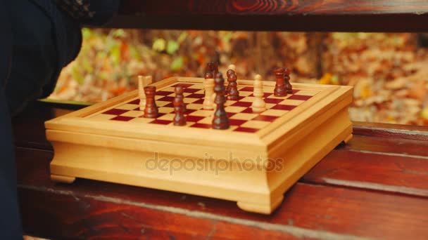 Старий грає в шахи один на лавці в осінньому парку — стокове відео