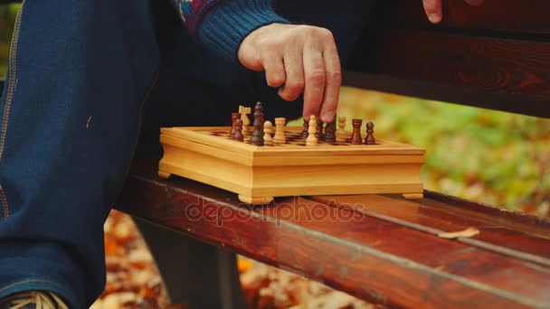 Vieil homme joue aux échecs seul sur le banc dans le parc d'automne — Video