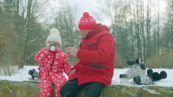 Petit garçon et son grand-père boivent du thé chaud après avoir patiné sur le lac — Video