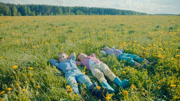 Tres niños pequeños están tumbados en la hierba y mirando las nubes en el cielo después del juego —  Fotos de Stock