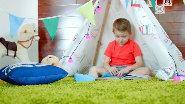 Küçük çocuk oyun odası onun kendi kendine yapılan Kızılderili çadırı kitap okuyor