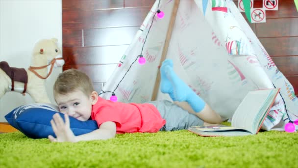 Kleine jongen is het boek lezen in zijn zelfgemaakte wigwam in de speelkamer — Stockvideo