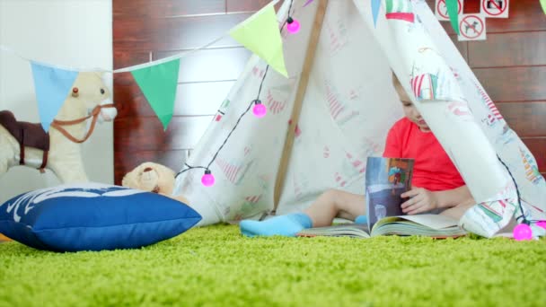 Little boy is reading book in his self made wigwam in playroom — Stock Video