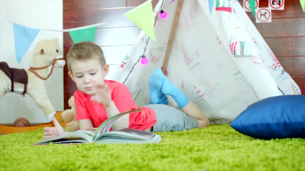 Menino está lendo livro em seu próprio wigwam feito na sala de jogos — Vídeo de Stock