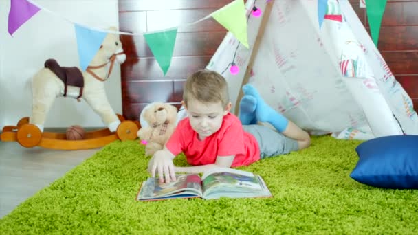 Mały chłopiec jest czytanie książki w swoim wigwamie selfmade w pokoju zabaw — Wideo stockowe