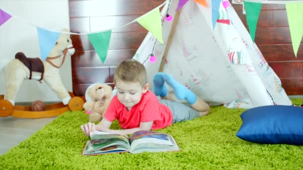 小さな男の子は、プレイルームで彼の自作のウィグワムで本を読んでいます — ストック動画