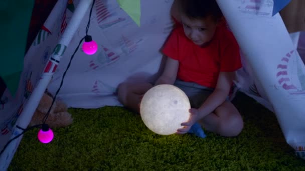 Liten pojke med leksak månen i händerna i själv gjort wigwam i lekrummet — Stockvideo