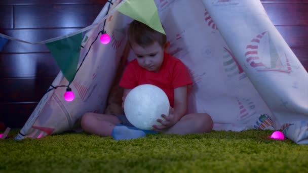 Little boy with toy moon in his hands in self made wigwam in the playroom — Stock Video
