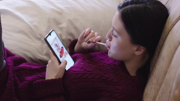 Een Jong Meisje Zuigen Een Lolly Zoek Smartphone — Stockvideo