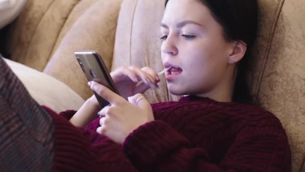 Młoda Dziewczyna Ssie Lizaka Patrzy Smartfona — Wideo stockowe