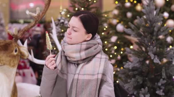 Een jonge vrouw die aan een lolly zuigt. Vrolijk meisje in kerstmis weekend veel plezier met snoep in haar handen. Kus snoep. Buiten, levensstijl. — Stockvideo