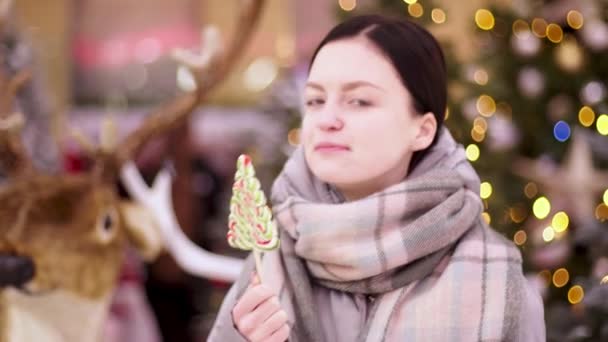 ロリポップを吸う若い女性。クリスマスの週末に陽気な女の子は彼女の手にキャンディーと楽しみを持っています。キスキャンディアウトドアやライフスタイル. — ストック動画