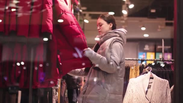 Mladá žena výběru oblečení na stojanu v showroomu — Stock video