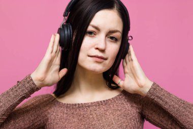 Pembe duvar arkasında izole edilmiş, kulaklıkla müzik dinleyen mutlu genç bir kadının görüntüsü.