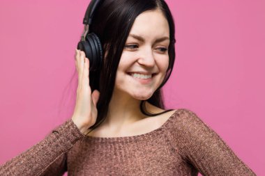 Pembe duvar arkasında izole edilmiş, kulaklıkla müzik dinleyen mutlu genç bir kadının görüntüsü.