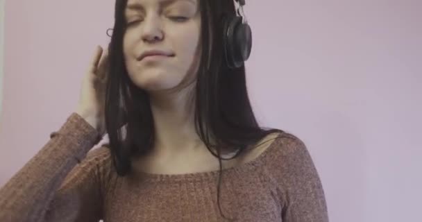 图片中 一个快乐的年轻美丽女子在粉红的墙壁上孤立无援 用耳机听着音乐 — 图库视频影像