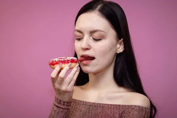 Retrato de cerca de una chica guapa complacida comiendo rosquillas aisladas sobre fondo rosa — Foto de Stock