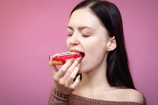 Крупным планом портрет довольной красивой девушки, поедающей пончики на розовом фоне — стоковое фото