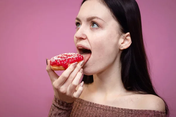 Retrato de cerca de una chica guapa complacida comiendo rosquillas aisladas sobre fondo rosa — Foto de Stock