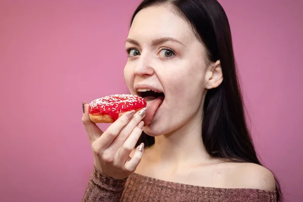 Крупным планом портрет довольной красивой девушки, поедающей пончики на розовом фоне — стоковое фото
