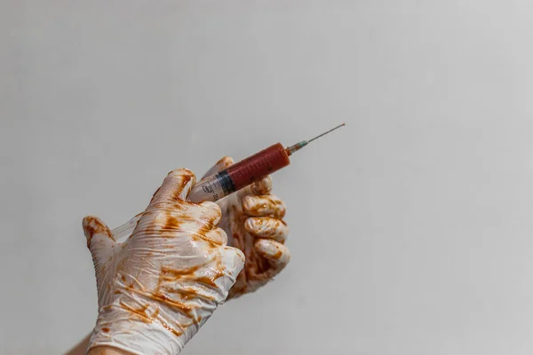 De arts houdt een spuit vast in latex handschoenen, handschoenen in het bloed — Stockfoto