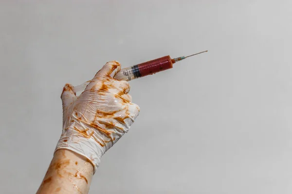 De arts houdt een spuit vast in latex handschoenen, handschoenen in het bloed — Stockfoto
