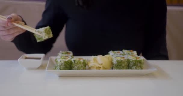 在餐馆吃寿司的女人，夏天中午拿着筷子吃鲑鱼寿司的年轻女人。吃传统食物的妇女的生活方式. — 图库视频影像