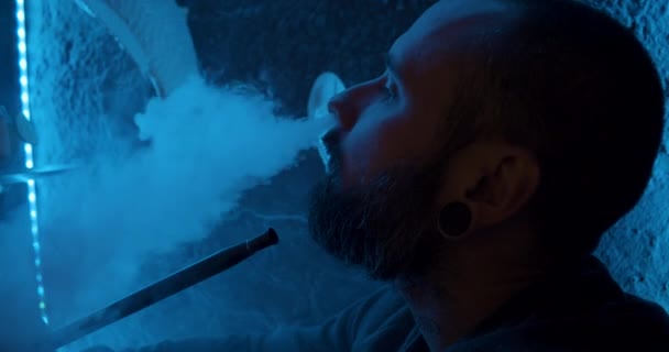 Een man met een baard die een hookah rookt in een donkere kamer. Hookah lifestyle en roken concept. portret van een zeeman met een hookah close-up uitzicht — Stockvideo