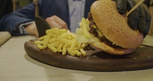 男ハンバーガーを食べるレストランがあり、彼は空腹と良い一口を持っています。ハンバーガー ディナー — ストック動画