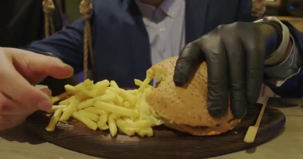 Homem em um restaurante comendo um hambúrguer, ele está com fome e tendo uma boa mordida. Jantar de hambúrguer — Vídeo de Stock