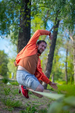 Genç adam ip üzerinde dengede duruyor ve zıplıyor. Yürüyen, zıplayan ve parkta ipte dengede duran bir adam..