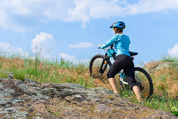 Ciclista femenina con su bicicleta de montaña subiendo por una roca a pie — Foto de Stock