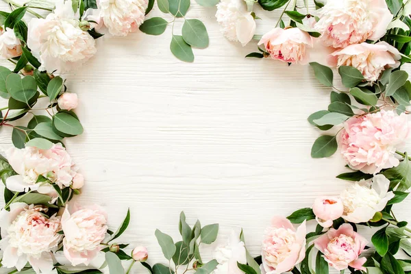 Floral pattern, frame made of pink peonies  branches of eucalyptus and leaves on wooden white background. Flat lay, top view. Valentine\'s background. Floral frame. Frame of flowers. Flowers texture