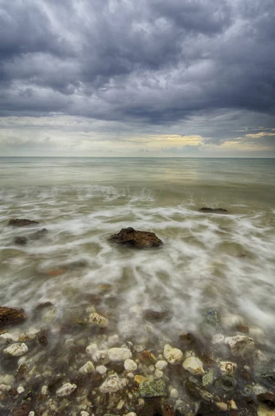 Enfoque suave e imagen borrosa pequeña ola golpeando la roca con nubes oscuras dramáticas — Foto de Stock