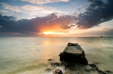 kıyı şeridi günbatımında. beton yapı su, güneş ışığı ile dramatik kara bulutlar terk. 