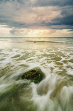 Yumuşak dalga sahilde yeşil yosun kaplı taş isabet ile çarpıcı günbatımı an