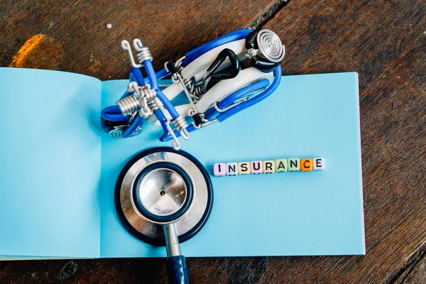 INSURANCE word block on note pad.handcrafted toy and used stethoscope. soft focus background