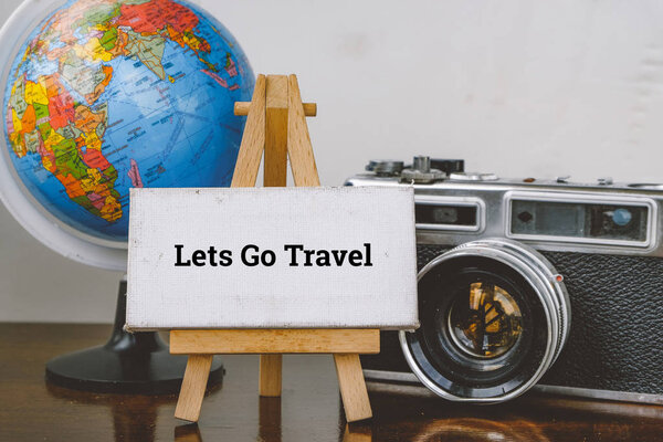 Travel and vacation concept image,word LETS GO TRAVEL and with easel ,globe and vintage camera layout on wooden desk.selective focus shot and faded effect