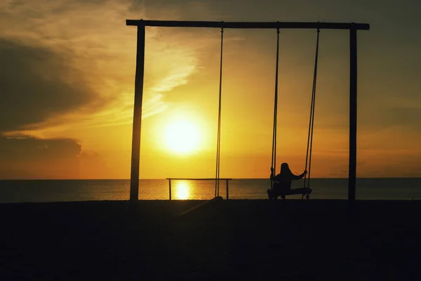 Silhouette of lonely girl with hijab on a swing with magical sun