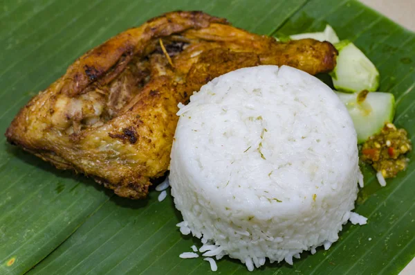 Автентична малайська страва, паровий рис, який подається з фритюрною курячою ногою, огірком та пастою чилі на банановому листі — стокове фото