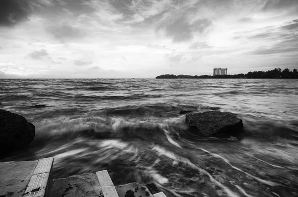 Schwarz-Weiß-Bild, weiche Wellenströmung, die den Sandstrand vor dunklem Wolkenhintergrund trifft. Weichzeichner-Bild durch Langzeitbelichtung — Stockfoto