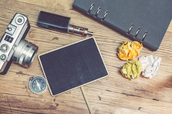 travel and vacation concept, top view of vintage camera, crumple paper,electronic cigarette and planner book layout on wooden floor.