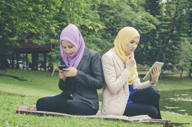 park ve okuma ebook üstünde onların hareket eden telefon, yeşil çimenlerin üzerinde oturan genç muslimah