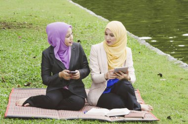 park ve okuma ebook üstünde onların hareket eden telefon, yeşil çimenlerin üzerinde oturan genç muslimah